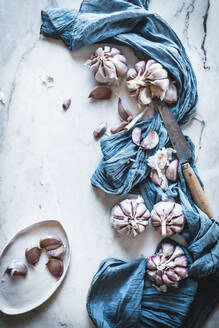 Cloves of unpeeled garlic served with blue napkin and ceramic plate placed on table in light kitchen - ADSF33720