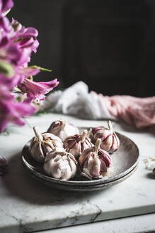 Cloves of unpeeled garlic on ceramic plate served with napkin on table in light kitchen - ADSF33723