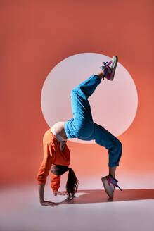 Ganzkörper-Seitenansicht einer aktiven Tänzerin, die eine anmutige Rad-Pose einnimmt und das Bein anhebt, während sie im Studio mit einem Kreis an der Wand tanzt - ADSF33727