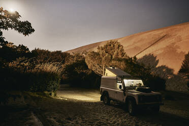 Illuminated off-road vehicle by sand dune at night - SSCF00956