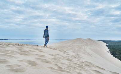 Woman walking on sand dune under cloudy sky - SSCF00959