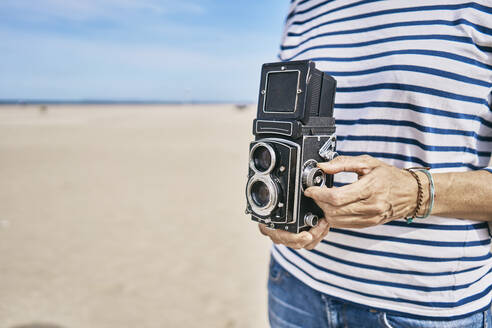 Woman with vintage camera standing at beach - SSCF01014