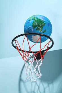 Round planet Earth with water and land in basketball hoop with colorful net on light background with sunlight and shadow - ADSF33743