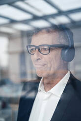 Thoughtful senior businessman with headphones in office - JOSEF07284