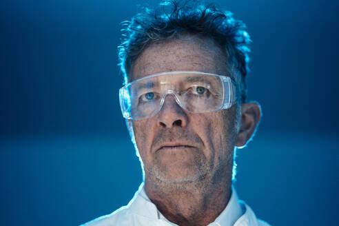 Nachdenklicher Wissenschaftler mit Schutzbrille vor einer blauen Wand - JOSEF07287