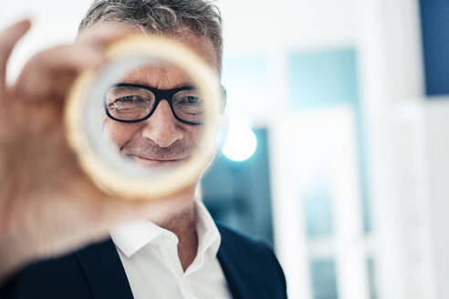 Lächelnder älterer Geschäftsmann mit Brille schaut durch ein kreisförmiges Objekt - JOSEF07296