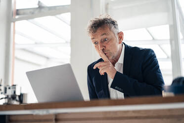 Senior businessman doing silence gesture on video call through laptop - JOSEF07304