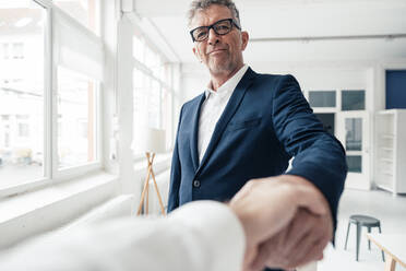 Smiling businessman shaking hand with colleague in office - JOSEF07307