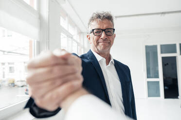 Smiling businessman holding hand of colleague at work place - JOSEF07309