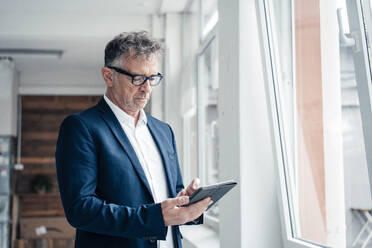 Businessman using tablet computer by window in office - JOSEF07313