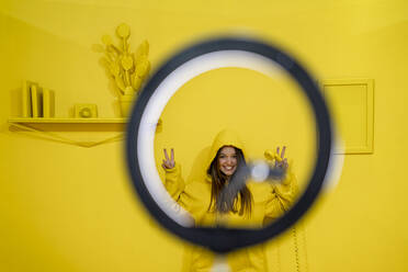 Happy woman smiling through ring light against yellow background - DLTSF02727