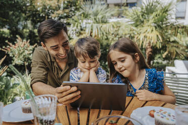 Vater und Kinder benutzen einen Tablet-PC im Hinterhof - MFF08580