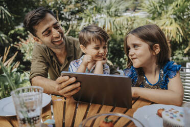 Glücklicher Vater und Kinder mit Tablet-PC im Garten - MFF08581