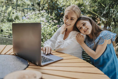 Mutter und Tochter führen ein Videogespräch über einen Laptop im Hinterhof - MFF08597