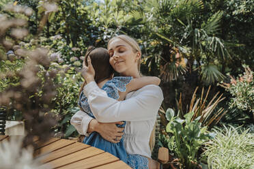 Smiling mother embracing daughter in back yard - MFF08599