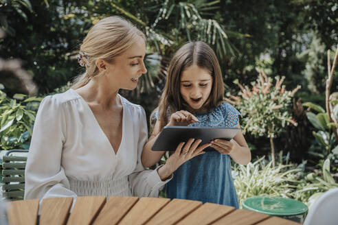 Happy mother and daughter using tablet computer at back yard - MFF08603