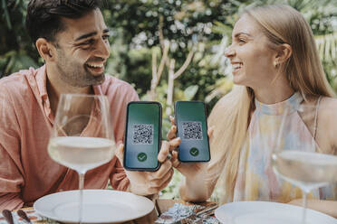 Glückliches Paar zeigt QR-Codes auf Smartphones im Restaurant - MFF08613