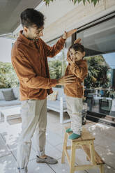 Father measuring height of son standing on stool in patio - MFF08628