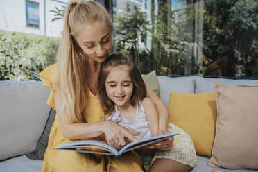 Mother and daughter reading a book sitting on sofa - MFF08635