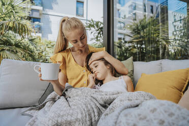 Mother taking care of her sick daughter sitting on sofa - MFF08637