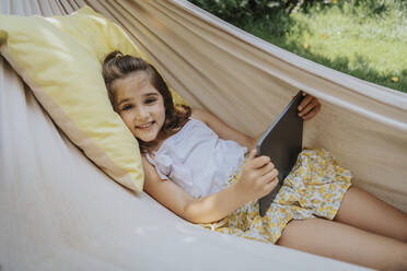 Lächelndes Mädchen mit Tablet-PC in der Hängematte im Hinterhof liegend - MFF08641