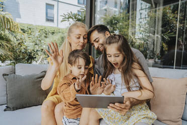 Familie winkt bei Videoanruf über Tablet-PC im Innenhof - MFF08646