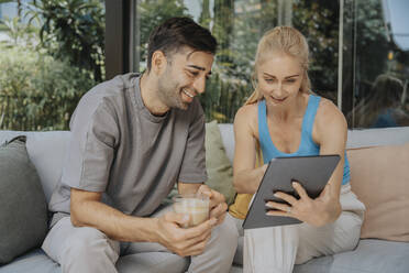 Frau, die ihr Smartphone mit einem Mann teilt, der in einer Lounge eine Kaffeetasse hält - MFF08655