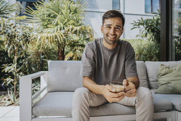 Happy man holding coffee cup sitting at lounge - MFF08660