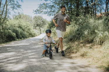 Father running by son cycling on road - MFF08669