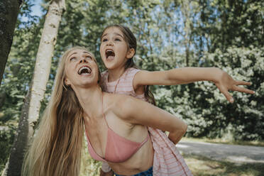 Cheerful mother giving piggyback ride to daughter in nature - MFF08673