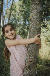 Cute girl making face holding tree trunk - MFF08675