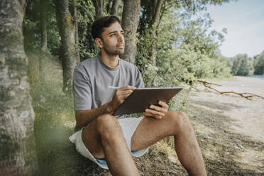 Thoughtful man with tablet PC sitting at tree - MFF08687