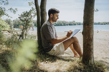 Mann benutzt Tablet-PC am Seeufer am Wochenende - MFF08689
