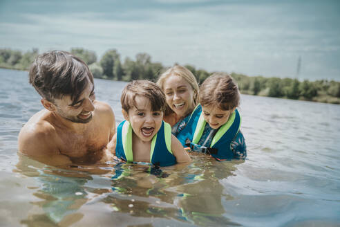 Fröhliche Eltern schwimmen mit Kindern im See - MFF08700