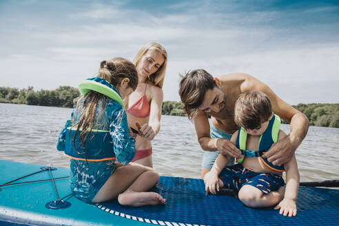 Eltern befestigen Schwimmweste für ihre Kinder im See - MFF08711