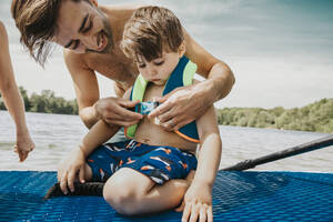 Vater befestigt Schwimmweste für Sohn im See - MFF08712