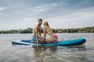 Glückliches Paar sitzt auf Paddleboard schwimmend über See - MFF08714
