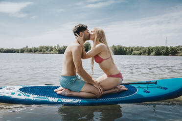 Frau küsst Mann, der auf einem Paddelbrett sitzt und über den See schwimmt - MFF08716