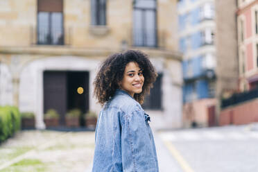 Smiling woman wearing denim jacket on street - DGOF02295