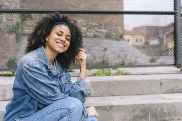 Happy young woman sitting on steps - DGOF02300