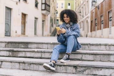 Lächelnde junge Frau mit Mobiltelefon auf einer Treppe - DGOF02313