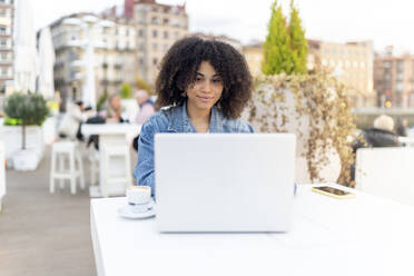 Afro junge Frau mit Laptop auf Tisch in Café - DGOF02341