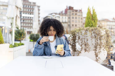 Junge Frau trinkt Kaffee und benutzt ihr Smartphone in einem Straßencafé - DGOF02342