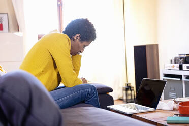 Worried woman with laptop sitting on sofa at home - EIF03466