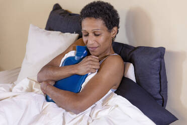 Woman holding hot water bag on bed at home - EIF03474