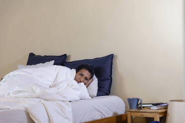 Frau auf dem Bett liegend, bedeckt mit einer weißen Decke, zu Hause - EIF03480