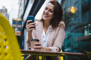 Glückliche Geschäftsfrau mit Smartphone in einem Straßencafé - AMWF00191