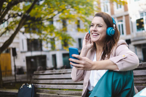 Happy woman listening music on headphones in park - AMWF00193