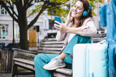 Smiling woman listening music and using smart phone on bench - AMWF00194