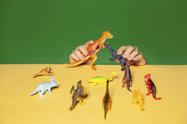 Hände des Mannes spielen mit Dinosaurier-Figur auf gelbem Tisch - IYNF00043